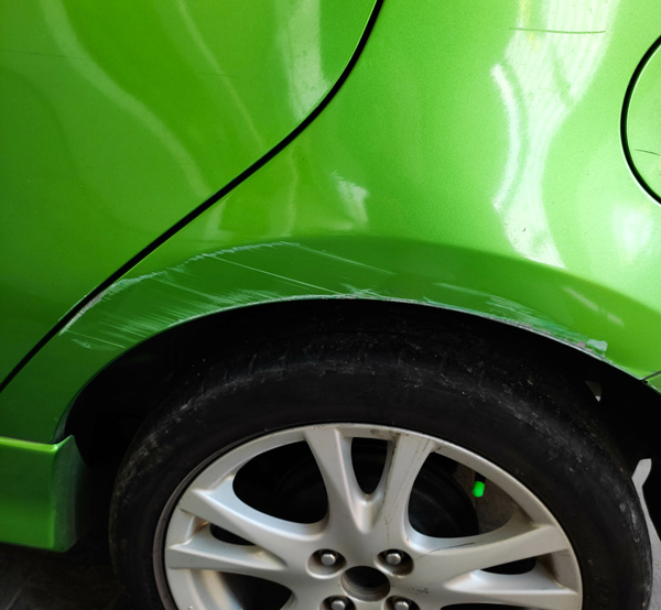 green car with scratched paint on rear fender revealing underlying damage and wheel showing a total of three visible blemishes