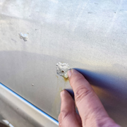 person touching automotive paint with damage and rust spots in need of repair options for restoration